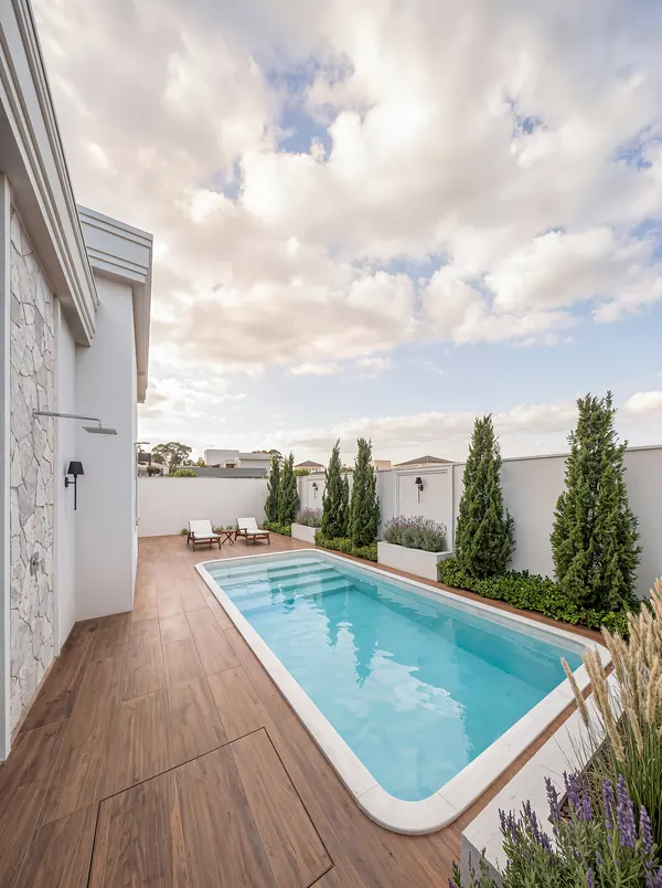 Deck de madeira com piscina aquecida, ciprestes e muro com arandelas